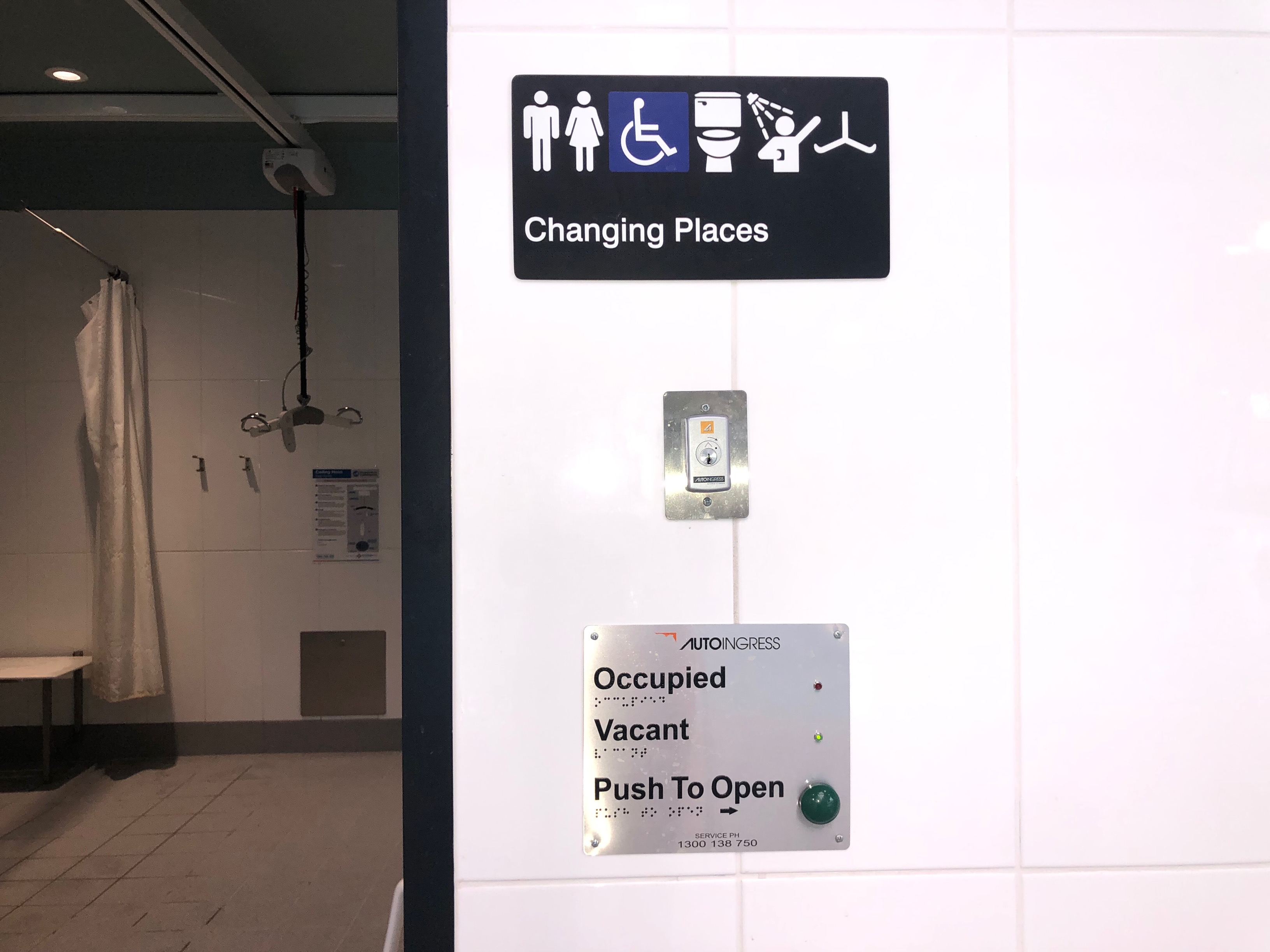 Image of signage to hoist change room with door open. Visible is the shower with privacy screens and entry signage featuring braille information.