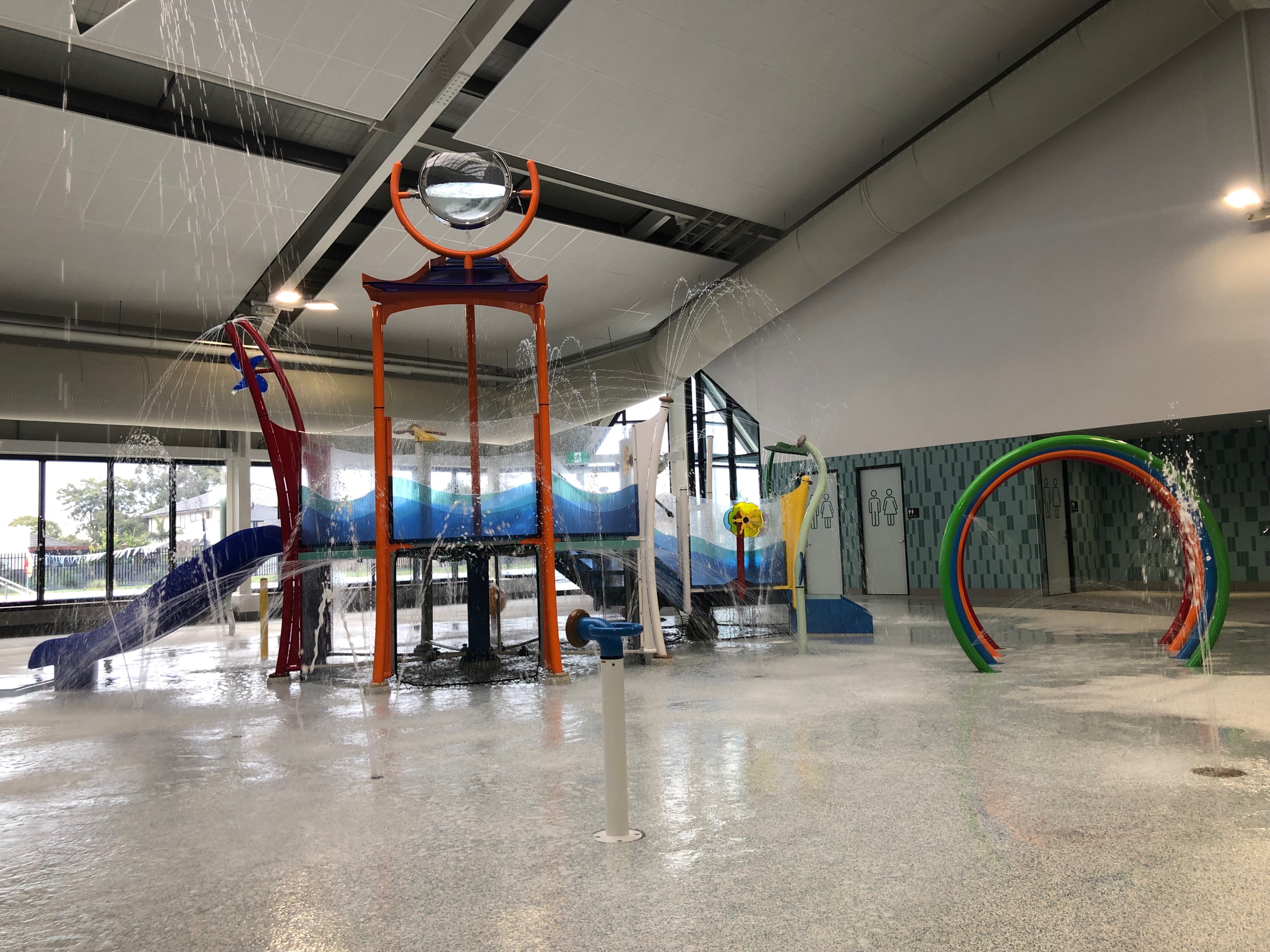 Image of the AquaPlay splash park featuring water ring tunnels, giant splash bucket, mini water slide and in-floor water sprinklers and bubblers