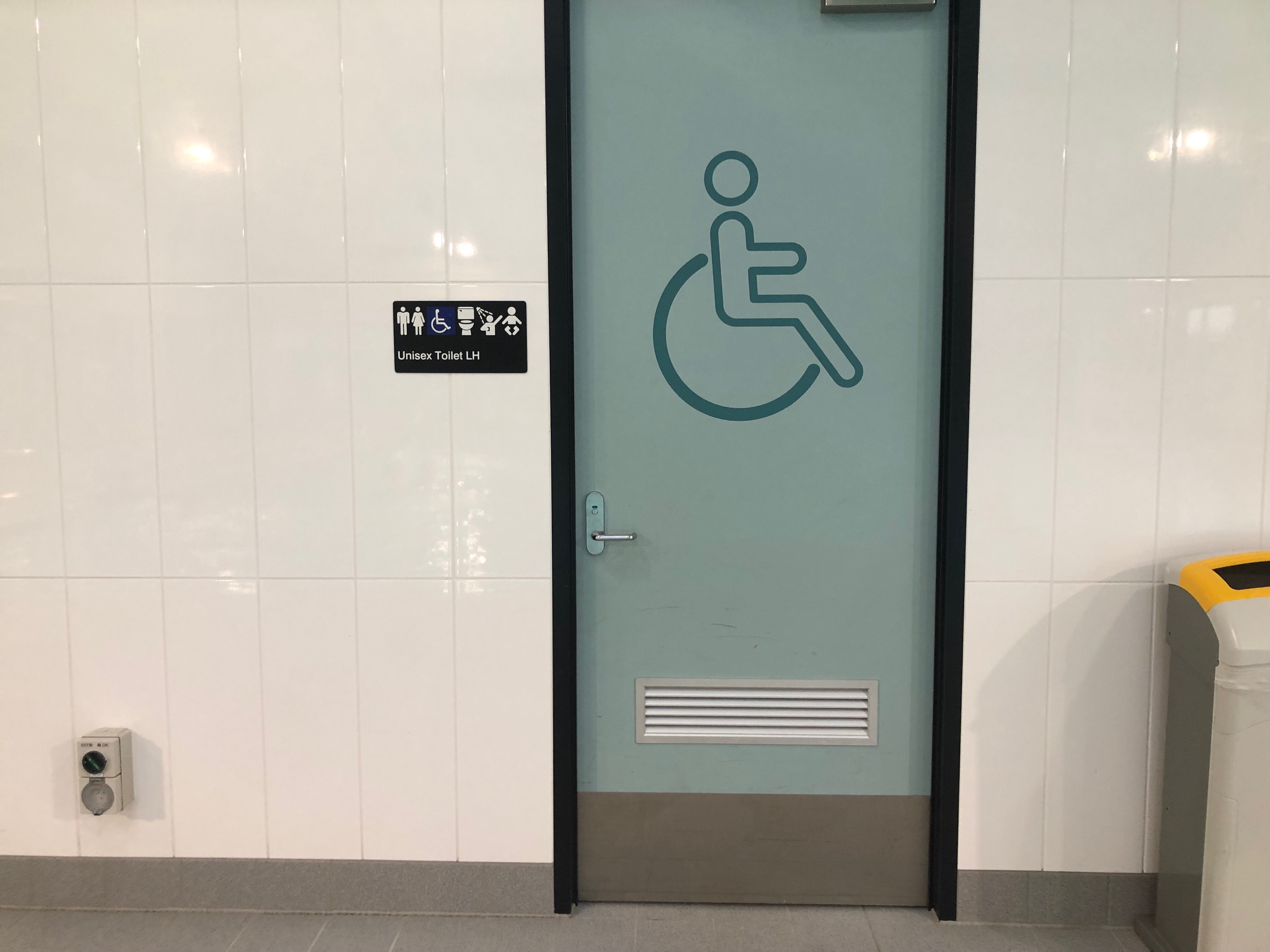Image of doorway to unisex wheelchair accessible changeroom featuring shower access, hand rails and infant changing table.